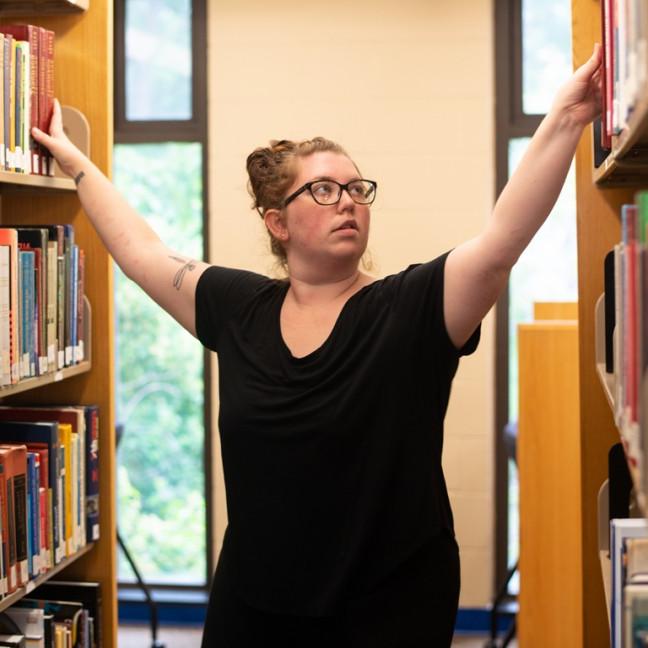 a student reaches for books on shelves on either side of her